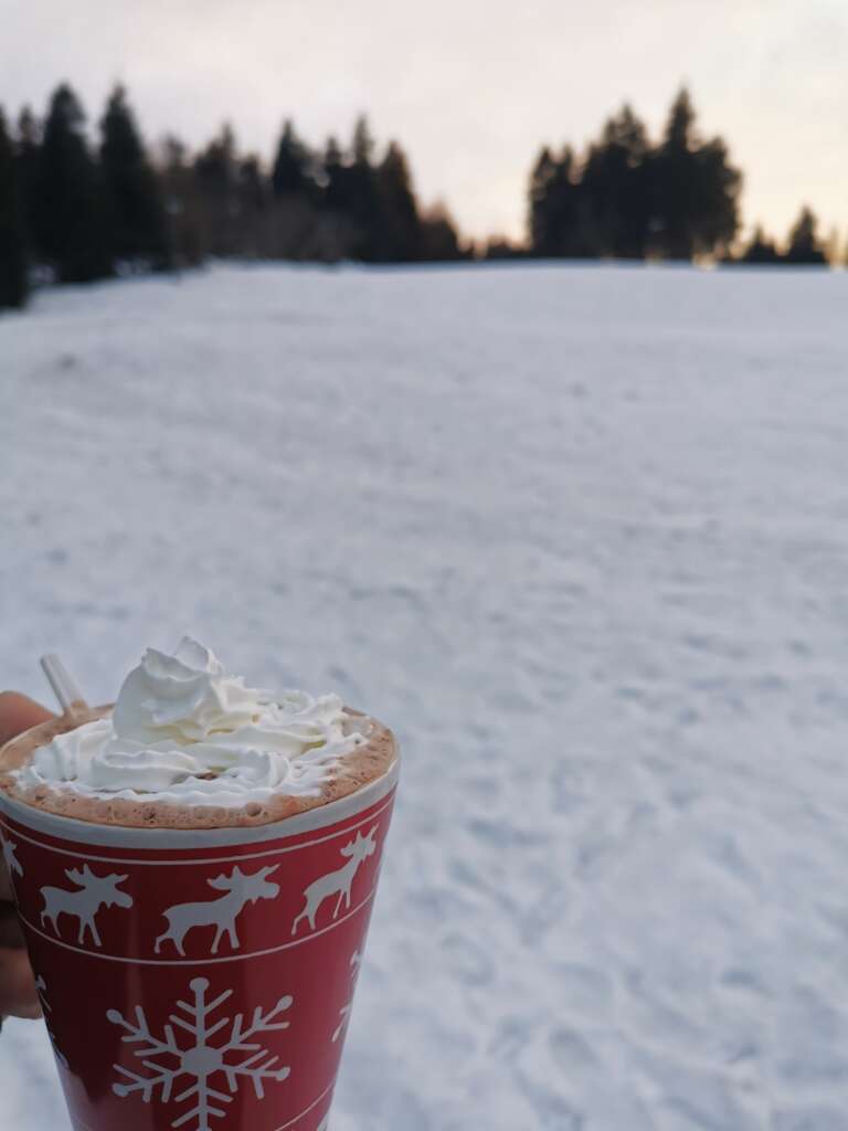 Becher mit heißer Schokolade und Sahne vor dem verschneiten Skihang
