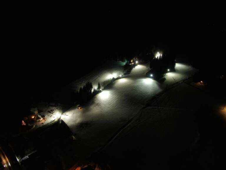 Der beleuchtete Skihang bei Nacht von oben