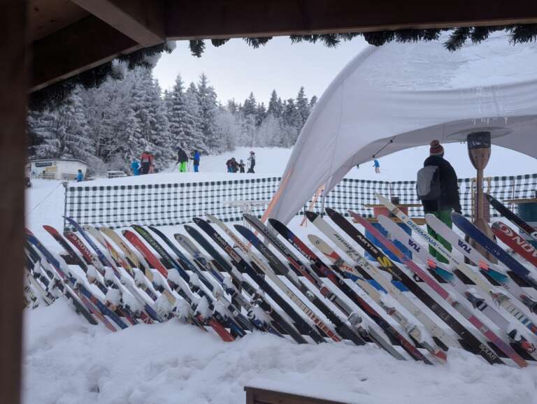Blick aus der Glühweinalm auf den Skihang, davor ein Zaun aus alten Skiern