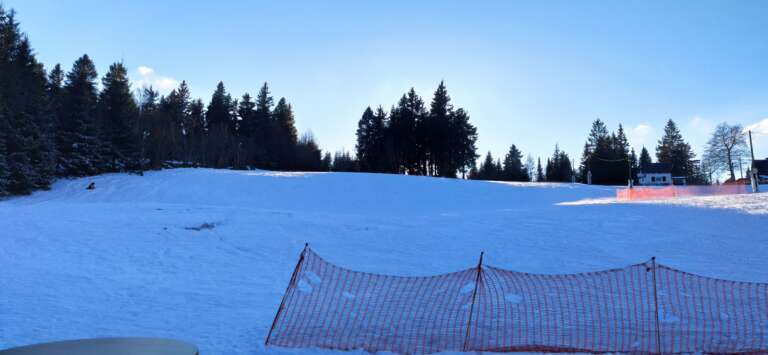 Verschneiter Skihang mit Fangnetz unter blauem Himmel