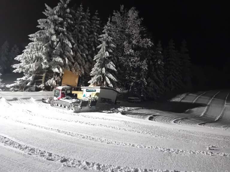 Präparierter Skihang bei Nacht vor verschneiten Tannen