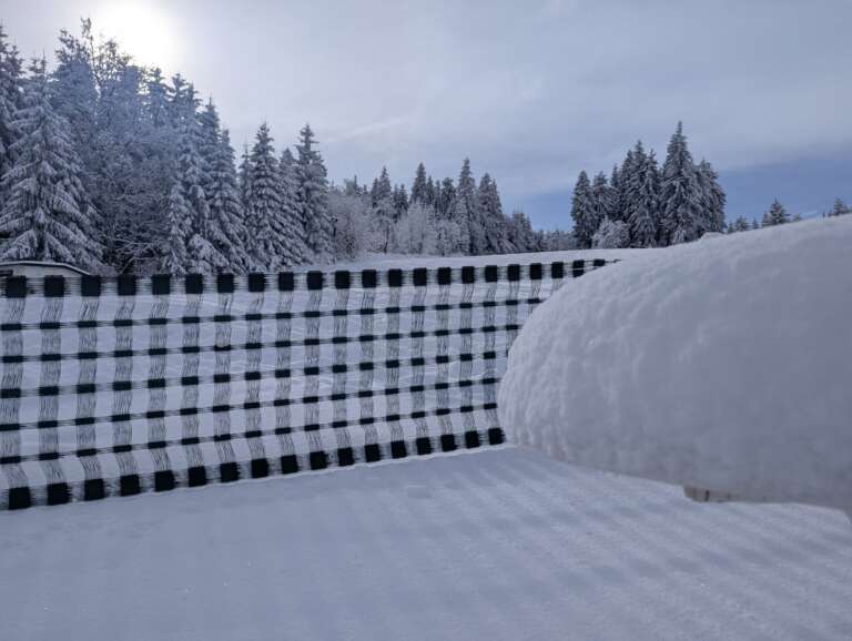 Dicke Schneehaube am Pistenzaun vor verschneiten Fichten