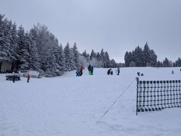 Gäste auf der Piste am Rotterhang vor verschneitem Winterwald